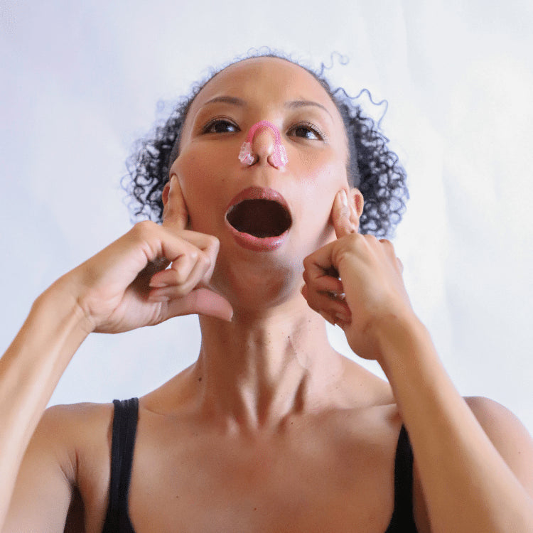 A woman demonstrating the use of the nose contouring clip from the GST Body face-scia kit, placed on her nose while she performs a facial exercise. Her fingers are positioned at the sides of her face to support the movement, illustrating how the tool helps shape and contour the nose naturally by engaging the facial muscles.