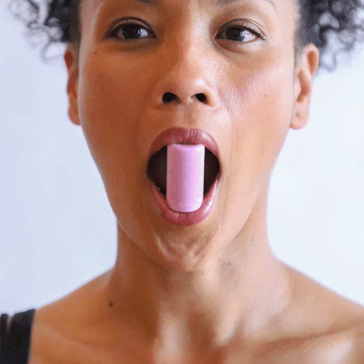 A close-up of a woman demonstrating the use of a pink cork decompressor tool from the GST Body face-scia kit. The tool is placed inside her mouth, gently decompressing the facial muscles around the lips and jaw, illustrating one of the fascia-focused exercises.